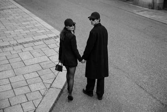 “Black-and-white photograph of two people in dark coats holding hands beside the water.”
