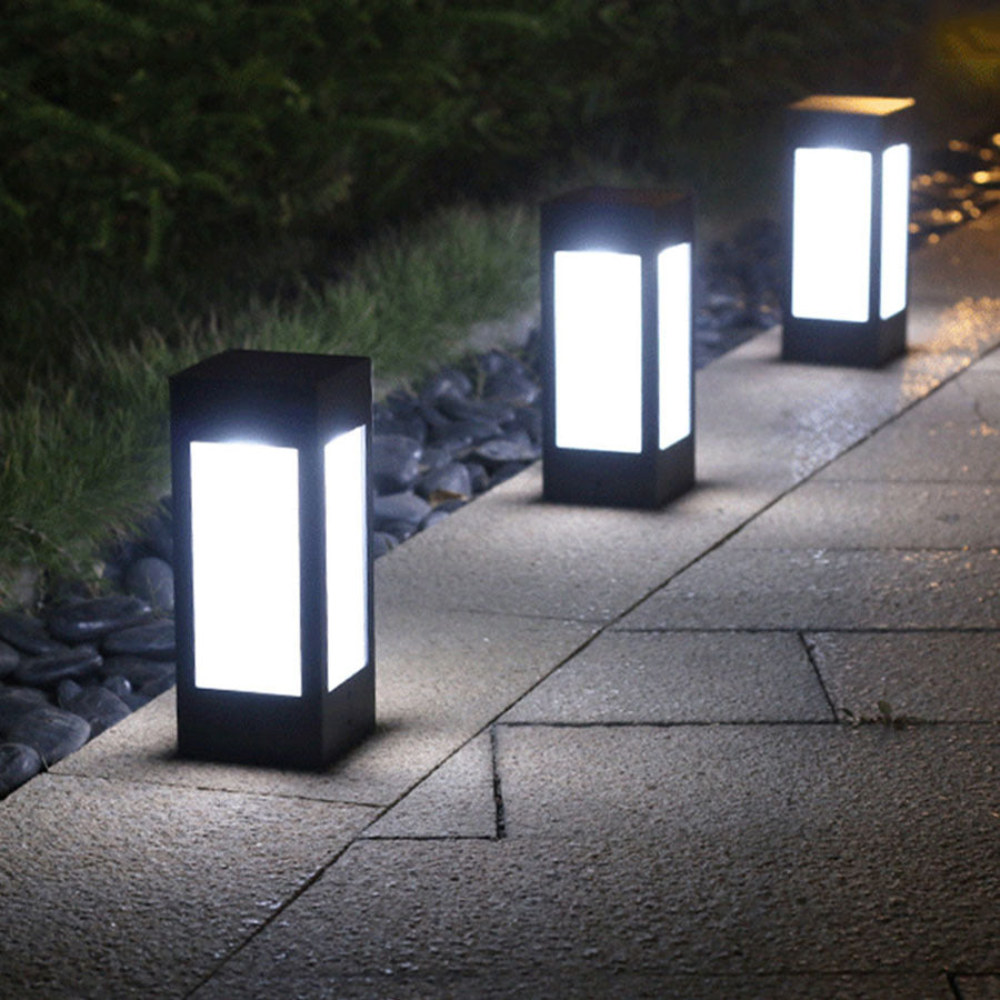 Two black tall solar lantern garden lights with frosted glass panels glowing on walkway