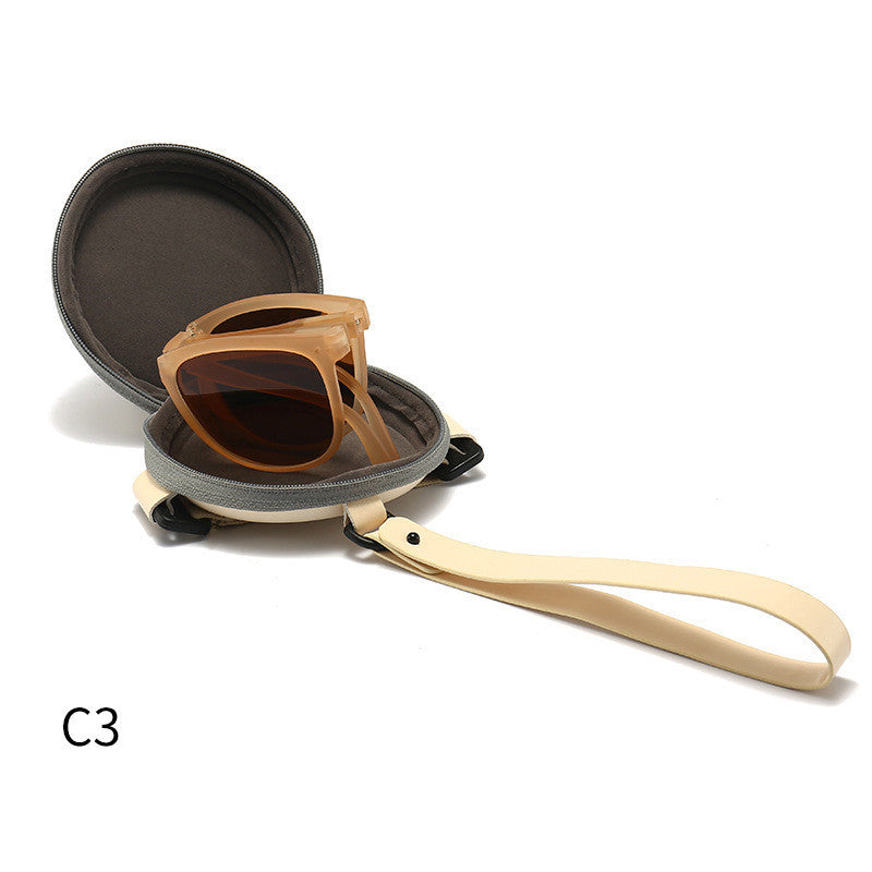 Foldable sunglasses with amber-brown frames and dark lenses, shown with hard case