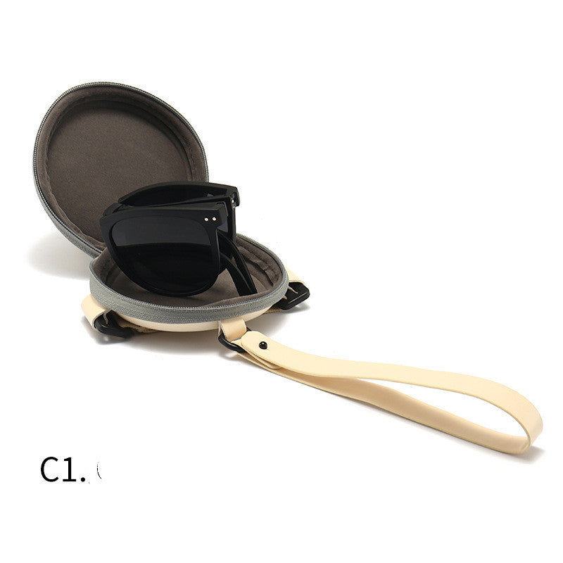 Foldable sunglasses with light tan frame, dark lenses, open round case beside