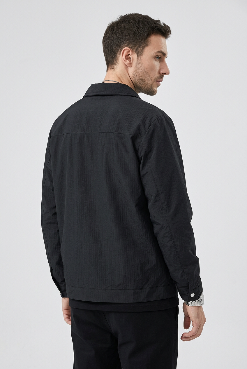 Slim male model wearing REEVEAR black snap-down jacket, rear three-quarter view